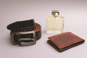 A set of accessories for a stylish man. Expensive perfume, leather belt, business card holder on a light gray background. Concept of fashion and style, lifestyle of male businessman.