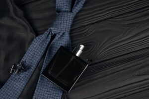 A bottle of mens cologne and cufflinks with blue tie lie on a black luxury fabric background on a wooden table. Mens accessories