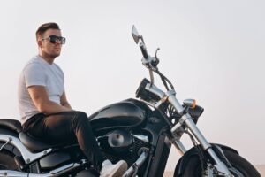 Portrait of a young attractive guy in sunglasses. Nice young man in a white T-shirt and black jeans on a motorcycle. Life style photography. Side view